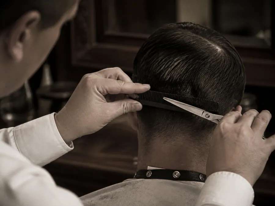Barbier arbeitet mit Kamm und Schere am Hinterkopf eines Gastes